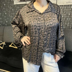 Leopardmönstrad blus - Snygg leopardmönstrad blus i glansigt material med långa ärmar och knappar framtill. Perfekt för en trendig look.