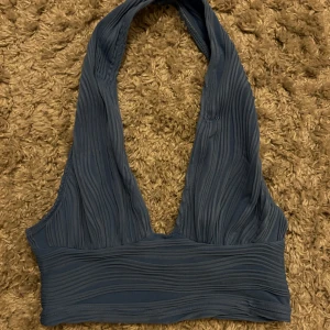 Mörkblå halterneck topp - Snygg mörkblå halterneck topp med ribbad textur. Perfekt för en stilren och modern look. Toppen har en djup urringning och är ärmlös, vilket gör den idealisk för varmare väder.