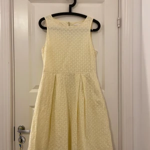 Gul ärmlös klänning - Charmig gul klänning med ett diskret mönster. Den är ärmlös och har en klassisk, feminin siluett med en rund halsringning. HAR FICKOR! Perfekt för vår och sommar.