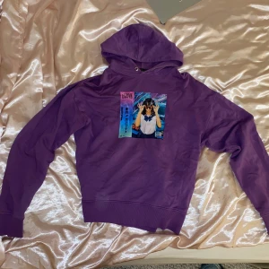 Lila hoodie med tryck - Cool lila hoodie med ett färgglatt tryck av en tjej i solglasögon. Perfekt för en avslappnad stil med en touch av retrovibbar. Hoodien har långa ärmar och en klassisk huva.