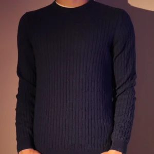 Mörkblå stickad tröja från Massimo Dutti - Säljer en stilren mörkblå stickad tröja från Massimo Dutti. Tröjan har ett klassiskt kabelstickat mönster och långa ärmar, perfekt för kyligare dagar. Passar både till vardags och mer uppklädda tillfällen.