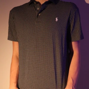 Mönstrad pikétröja från Ralph Lauren - Snygg pikétröja från Ralph Lauren med ett diskret mönster i svart och vitt. Tröjan har korta ärmar och en klassisk krage med knappar. Perfekt för en stilren look. Frånvarande lapp.