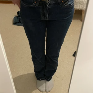 Mörkblå jeans - Säljer ett par klassiska mörkblå jeans med låg midja och straight passform. Perfekta för en avslappnad stil. De har en traditionell femficksdesign och stängs med dragkedja och knapp. Byxorna är uppsprättade längst ner. 