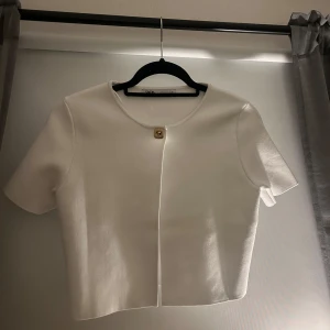Vit kortärmad kofta från Zara - Snygg vit kortärmad lofta från Zara med en enkel knappdetalj framtill. Perfekt för en stilren look. Aldrig använd men saknar tyvärr prislapp.
