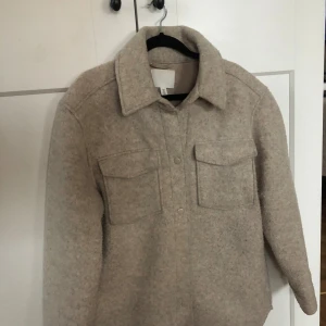 Beige overshirt från H&M - Säljer en stilren beige overshirt/Jacka från H&M. Jackan har långa ärmar och två bröstfickor med knappar. Perfekt  under höst och vår/vinter 