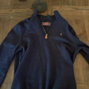Mörkblå halfzip tröja  från Morris - Säljer en stilren mörkblå tröja från Morris i 100% merinoull. Tröjan har en praktisk dragkedja framtill och en liten broderad logga på bröstet. Perfekt för kyligare dagar. Obs tröjan är lite liten i storleken