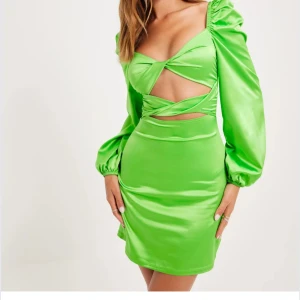 Grön klänning från NLY Trend - Snygg grön klänning från NLY Trend med lång ärm och en cool cut-out design framtill. Klänningen har en kort längd och är tillverkad i ett glansigt material som ger en lyxig känsla. Endast testad, men har defekter vid dragkedjan som syns på bild 3.