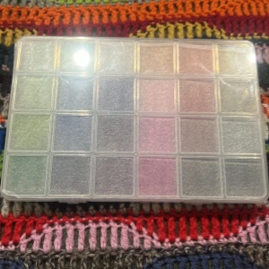 Färgglada pärlor i förvaringslåda - En praktisk förvaringslåda med ett brett utbud av små, färgglada pärlor. Perfekt för smyckestillverkning eller pyssel. Lådan har flera fack som håller pärlorna organiserade och lättillgängliga.