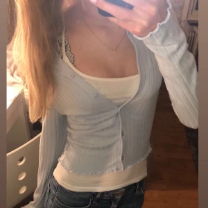 Ljusblå ribbad kofta - Säljer en ljusblå ribbad kofta med knappar framtill. Koftan har långa ärmar och en v-ringad design, perfekt för lager-på-lager-stil. Passar bra till både jeans och kjol.