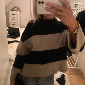 Randig stickad tröja från Ginatricot - Säljer en snygg randig tröja från Ginatricot i beige och svart. Tröjan är croppad med långa ärmar och en hög krage. Säljer då den inte kommer till användning 