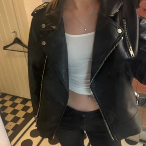 Svart skinnjacka från Zara - Snygg svart skinnjacka från Zara med dragkedjor och knappar. Jackan har långa ärmar och en klassisk bikerstil.