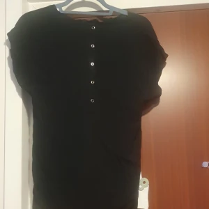 Svart kortärmad topp med knappar - Säljer en svart kortärmad topp med knappar baktill . Perfekt för en avslappnad stil. Toppen har en enkel design och är lätt att matcha med olika outfits.