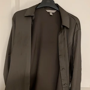 Olivgrön skjorta - Stilren olivgrön skjorta med knappar framtill. Skjortan har långa ärmar och en klassisk krage, perfekt för en elegant look.