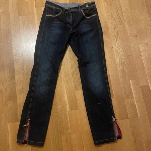 Mörkblå jeans med detaljer från Cappopera - Snygga mörkblå jeans från Cappopera med unika detaljer. Byxorna har broderade mönster på bakfickorna och glittrande stenar längs fickorna och bensluten. Byxorna har tyvärr blivit för små. Sitter bra på en tjej med storlek xs/s💞Jag är 164 och de går precis ner till marken i längden.