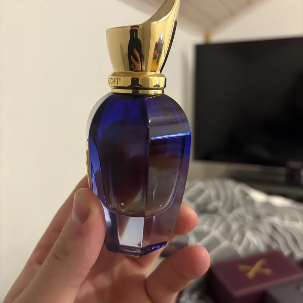 Elegant parfymflaska i en djupblå nyans med en gyllene kork. Flaskan har en unik, facetterad design som ger ett lyxigt intryck. Kommer i en stilren, mörklila förpackning med guldfärgad logotyp.. Perfume.