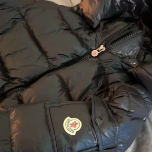 Moncler Maya Jacka - Snygg svart dunjacka från Moncler med dragkedja och knappar. Jackan har en quiltad design och Moncler-logga på armen. Jackan har NFC scan. 