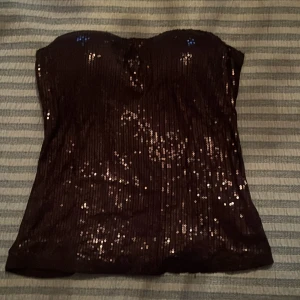 Svart paljettprydd tubtopp - Snygg svart tubtopp med glittrande paljetter, perfekt för en festlig kväll. Perfekt nu till nyår! Den har ett litet hål som säkert går att laga (bild tre) och så har lite paljetter lossnat men inget man tänker på❣️❣️