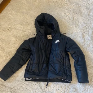 Jacka från Nike - Snygg svart pufferjacka från Nike med huva och dragkedja. Storlek S 