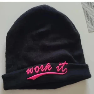 Svart mössa från Glitter - Snygg svart mössa från Glitter med texten 'work it' broderad i rosa framtill. Perfekt för att hålla värmen under kyliga dagar.