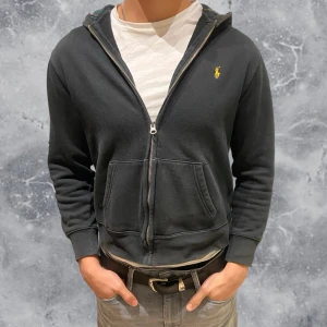 Ralph Lauren Zip Hoodie svart  - •Ralph Lauren Full Zip Hoodie med rutig luva. Skick: 6-7/10, två små skador på höger sida av plagget, ej märkvärdigt(se bild) Storlek: 14/16 yrs= sitter som strl 160 cm. •Mått | axel neråt: 51,5 cm. Bredd: 43 cm. Modell: 173 cm, 63 kg drygt(sitter för litet på bild) Authentic: ✅ Mvh Hessler’s