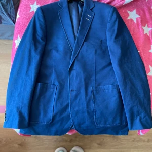 Blå kavaj från Sergio Rossi - Snygg blå kavaj från Sergio Rossi med klassisk design. Kavajen har två framfickor och en bröstficka. Perfekt för både formella och semi-formella tillfällen. Ett stilrent val för garderoben! Den har dock ett inte så synlig gul streck vid höger armen.