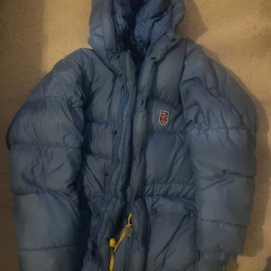 Blå dunjacka från Fjällräven - Säljer en blå fjällräven jacka! Dragkedjan har gått av men följer med i en ficka. Ev fläckar på jackan kan finnas men går nog bort i tvätten😊