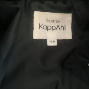 Svart pufferjacka från KappAhl - Säljer en svart pufferjacka från KappAhl med dragkedja framtill. Jackan har en quiltad design och är perfekt för kyligare väder. Den är både stilren och funktionell.