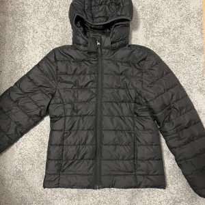 Svart pufferjacka från H&M - Säljer en svart pufferjacka från H&M med huva och dragkedja. Jackan är perfekt för kyligare dagar och har en stilren design. Den är lätt och bekväm att bära. (Barn jacka storlek 152)