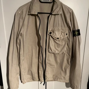Stone Island Overshirt  - Säljer en beige jacka från Stone Island med dragkedja och en bröstficka. Den är köpt på NK i Stockholm 2022 Box följer med!