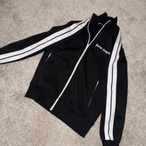 Svart tracksuit från Palm Angels - Con: Avgör själva! General wear, har fått sig 2 fläckar på höger sida av byxorna som i princip inte syns när man har på sig dom, samt att bokstäverna ”A” o ”N” har lossnat på insidan av byxorna. Annars inga flaws alls.  Båda är i strl M  Säljer det i par  Köpta på Palm angels hemsida, dvs orderbekfräftelsen följer med om man så vill. Köparen står för frakt
