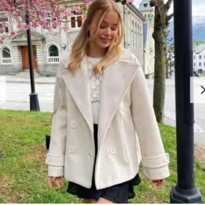 Vit kappa med knappar - Snygg vit kappa med stora knappar och bred krage. Perfekt för vår och höst. Den har en stilren design med långa ärmar och en lös passform. Däremot har den en reva inuti men inget som man ser de är lätt att sy igen!