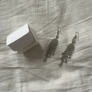 Glittriga silverörhängen - Snygga och eleganta glittriga örhängen i silverfärg. De har en hängande design med flera rader av gnistrande stenar som ger en lyxig känsla. Perfekta för att lyfta vilken outfit som helst.pris kan diskuteras 