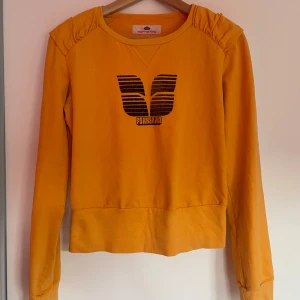 Gul långärmad tröja från Fornarina - Säljer en snygg gul långärmad tröja från Fornarina med ett svart tryck på framsidan. Tröjan har rynkade detaljer vid axlarna och en rund halsringning. Mycket sparsamt använd! ☺️
