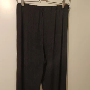 Svarta byxor med resårmidja - Snygga svarta byxor med resårmidja för en bekväm passform. Perfekta för en stilren look och kan enkelt matchas med olika toppar. Materialet ser ut att vara mjukt och följsamt. Säljer dessa då de inte kommer till användning mer. Svarta byxor med gummiband i midjan. Står ingen storlek, men skulle nog säga L eller one size.  Det är ett material, som görr att jag tycker det är finbyxor. Lite glans i tyget. Tunna!  Märke: okänt Byxorna är använda, men tycker att de är i mycket bra skick.