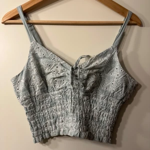 Ljusblå broderad linnetopp - Söt ljusblå linnetopp med broderade detaljer och smala axelband från Twist & Tango. Knytning framtill och en elastisk, smockad nederdel som gör den flexibel i storlek. Justerbara axelband. Utan anmärkningar 🩵