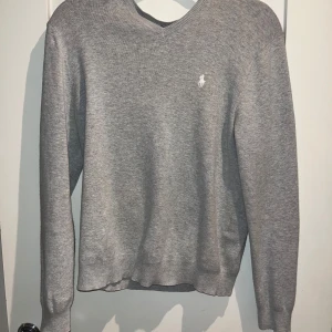 Grå tröja från Polo Ralph Lauren - Säljer en stilren grå tröja från Polo Ralph Lauren i 100% bomull. Tröjan har en klassisk v-ringning och det ikoniska logotypbroderiet på bröstet. Perfekt för en avslappnad men ändå elegant look.