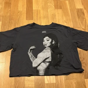Svart t-shirt med Ariana Grande-tryck från H&M - Cool svart t-shirt från H&M med ett stort tryck av Ariana Grande på framsidan. Perfekt för fans av popstjärnan! T-shirten har en avslappnad passform och korta ärmar.