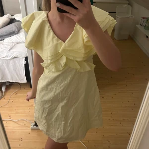 Gul klänning med volanger - Charmig gul klänning med volanger och öppen rygg. Den har en knytning i nacken och korta ärmar. Perfekt för sommarens festligheter! Köpt oanvänd på plick och ingen lapp så vet inte vart den är ifrån