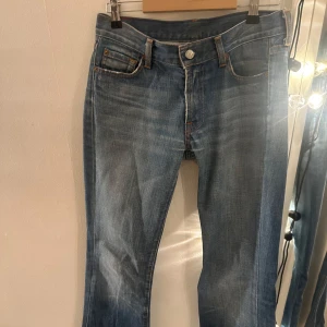 Blå jeans med slitna detaljer - Säljer ett par blå jeans med snygga slitna detaljer. De är förstörda längst ner då de har varit för långa för mig men man kan klippa av de om de skulle va. De är från all by markind och är mycket low waist och bootcut. Skicka för frågor😊