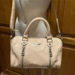 Beige axelväska med dragkedjor - Bilder från förra ägaren! Snygg Zadig väska köpt på Plick. Är lite sliten på handtagen. Vid intresse skickar jag detaljbilder. 