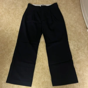 Mörkblå randiga kostymbyxor från Gina Tricot - Snygga mörkblå randiga kostymbyxor från Gina Tricot med diskreta ränder. Byxorna har en klassisk design med hög midja och vida ben, perfekt för en stilren look.