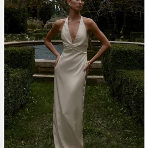 Krämvit långklänning - Superfin långklänning i satin från NAKD. Helt slutsåld på hemsidan!! Denna är endast testat och har kvar prislappen!! Storlek 36 och passa mig som är 165cm 💕💕💕 Perfekt till balen!!!