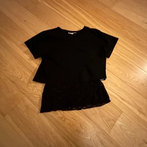 Svart kortärmad topp med spetsdetalj - Snygg svart topp med korta ärmar och en unik spetsdetalj nedtill. De är ett line och en kort t-shirt. Som sitter ej ihop