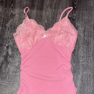 Rosa spetslinne från Shein - Säljer ett sött rosa linne från Shein med spetsdetaljer och smala axelband. Perfekt för en romantisk look eller som ett lager under en kavaj. Linnet har en liten rosett framtill som ger en extra touch.