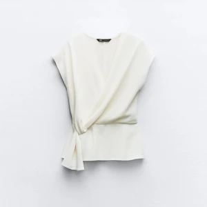 Vit topp från Zara - Snygg vit omlottopp från Zara med knytning i sidan. Toppen har en elegant v-ringning och korta ärmar, perfekt för en stilren look.