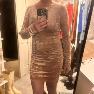 Ljusrosa sammetklänning - Snygg rosa klänning i sammet med långärmad design. Den har en tight passform och är perfekt för en elegant look. Klänningen är kort och har en mjuk, glansig yta som ger en lyxig känsla.