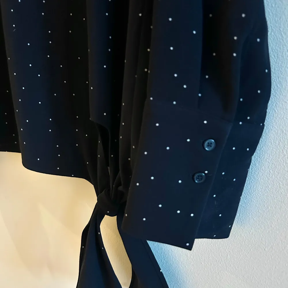 Säljer en stilren mörkblå tröja från Opus med små vita prickar. Tröjan har långa ärmar med skortknäopning och motveck. En knytning framtill på sidan ger tröjan en snygg detalj. Perfekt för en chic, lite mer dressad vardagslook!. Neuletakit & Villapaidat.
