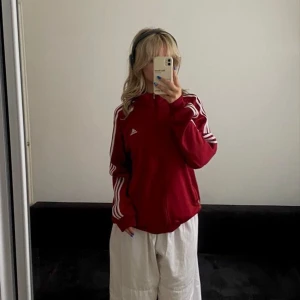 Röd träningsjacka från Adidas - Snygg röd träningsjacka från Adidas med de klassiska tre vita ränderna längs ärmarna. Jackan har dragkedja och Adidas-logga på bröstet. Perfekt för sportiga aktiviteter eller en avslappnad stil.