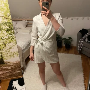 Jumpsuit omlott  - Vit jumpsuit med smala svarta ränder, långärmad, ser ut som en kostymklänning men är en jumpsuit 