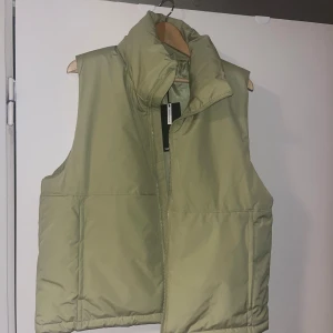 Ljusgrön dunväst med dragkedja - Snygg ljusgrön dunväst med hög krage och dragkedja framtill. Perfekt för kyligare dagar och enkel att matcha med olika outfits. Nyskick.